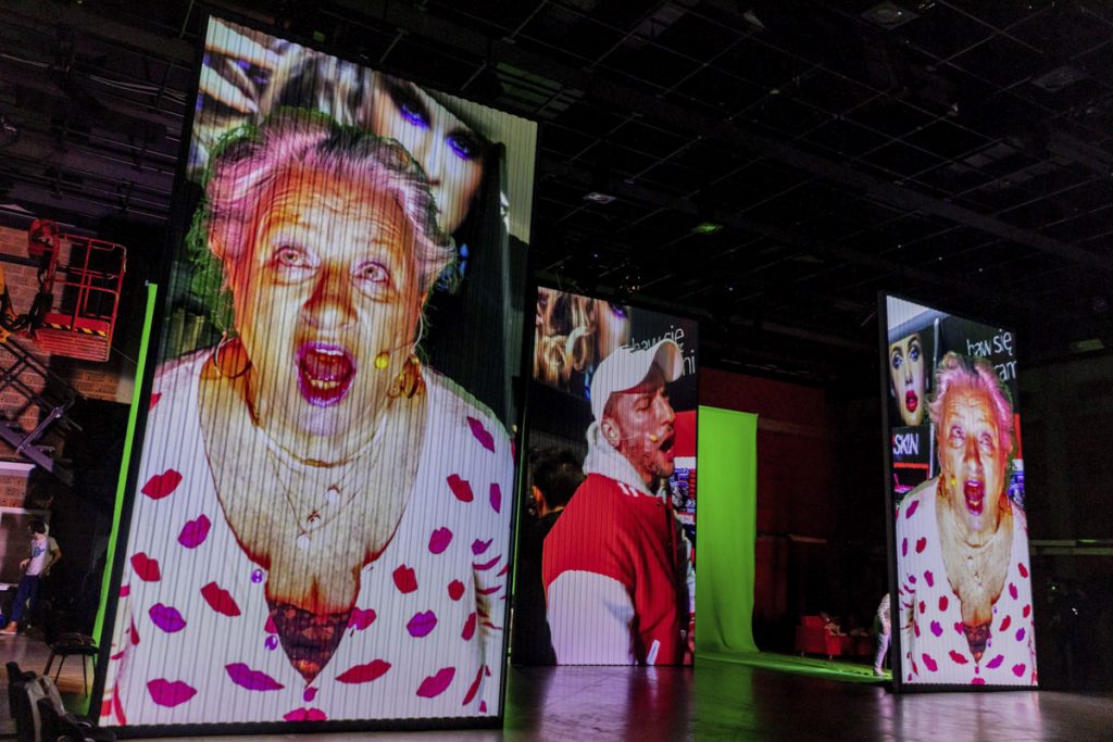 Na scenie stoją trzy ekrany. Na dwóch skrajnych widać tę samą projekcję krzyczącej starszej kobiety. Miedzy nimi ekran z krzyczącym młodym mężczyzną.