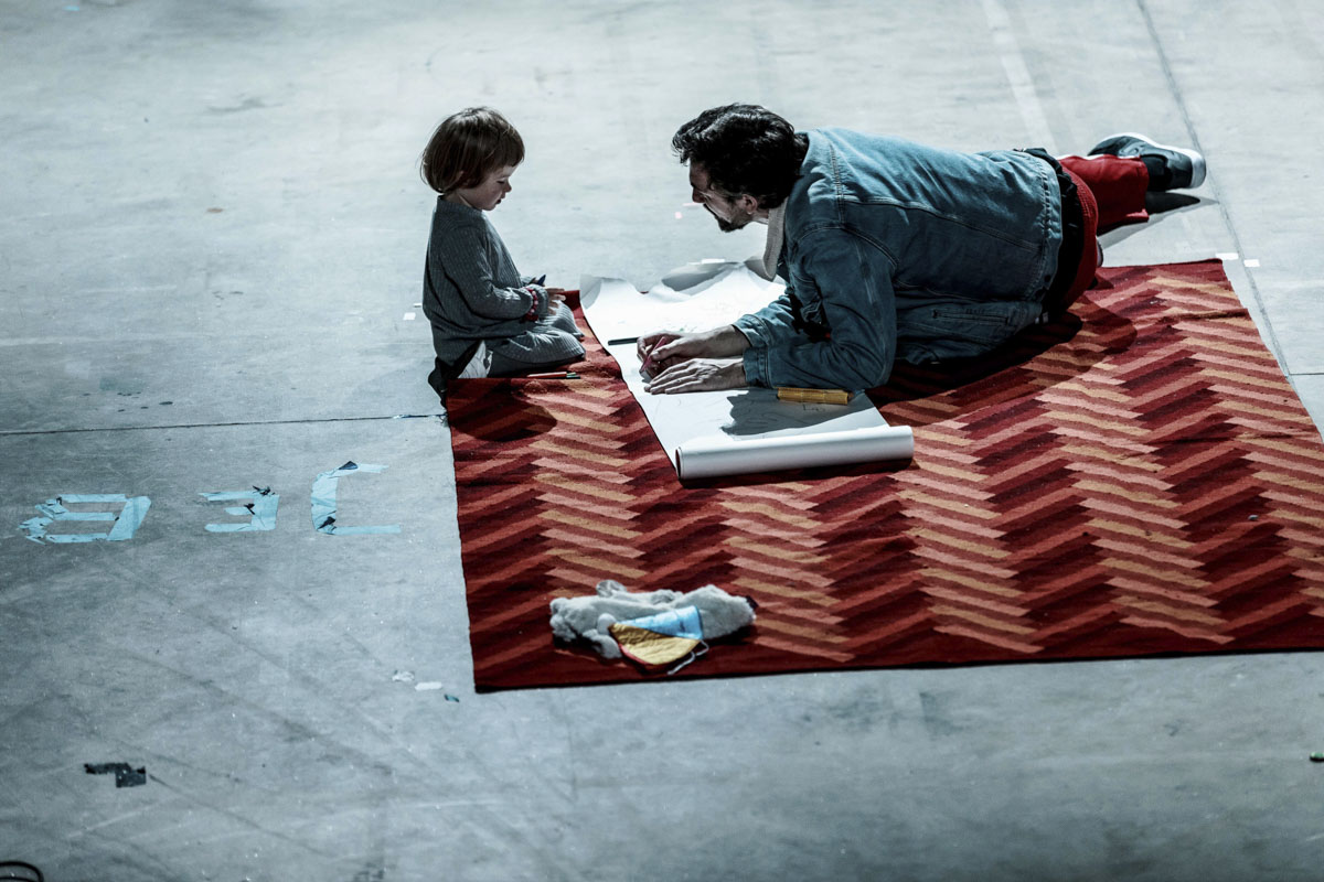Mężczyzna i mała dziewczynka bawią się na dywanie. Między nimi leży arkusz papieru, kredki.